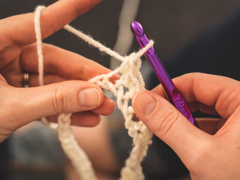 Someone uses a crochet hook with white yarn
